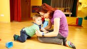 Baby spielt mit Betreuerin auf dem Boden im Happy Club des Familienhotels Ramsi in Kärnten