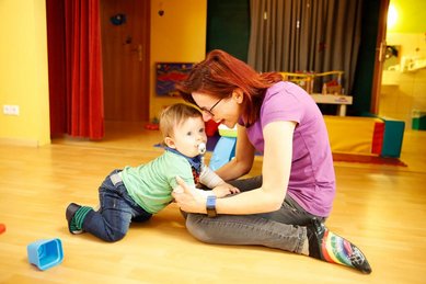 Baby spielt mit Betreuerin auf dem Boden im Happy Club des Familienhotels Ramsi in Kärnten