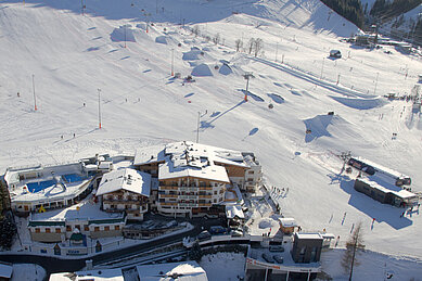 Winter Luftaufnahme vom Familienhotel Wellness- & Familienhotel Egger in Saalbach Hinterglemm mit Skipiste.