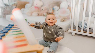 Baby sitzt im Familienhotel Friedrichshof in Bayern in einem hellen Spielbereich mit weicher Spielmatte und Kuscheltieren.