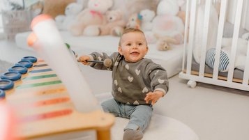 Baby sitzt im Familienhotel Friedrichshof in Bayern in einem hellen Spielbereich mit weicher Spielmatte und Kuscheltieren.