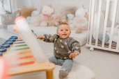 Baby sitzt im Familienhotel Friedrichshof in Bayern in einem hellen Spielbereich mit weicher Spielmatte und Kuscheltieren.