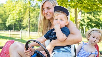 Mutter fährt mit ihren beiden Kindern eine Runde im Kettcar über das Außengelände des Landhuus Laurenz im Münsterland.