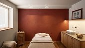 Ein gemütlicher Massageraum im Familienhotel Bella Vista in Südtirol mit Behandlungsliege, warmen Farben und Holzmöbeln.