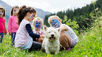 Kinder mit bemalten Gesichtern streicheln einen Hund im Familienhotel Kaiserhof an der Tiroler Zugspitzarena.