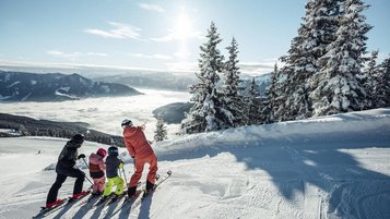 Eine Familie steht auf Skiern am verschneiten Hang und genießt den winterlichen Ausblick in der Bergwelt rund um das Familienhotel Amiamo