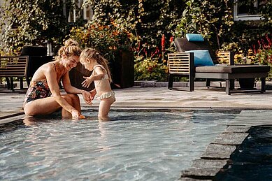 Mutter planscht gemeinsam mit ihrer Tochter im Kinderbecken des Außenpools im Familienhotel Landhaus Averbeck in der Lüneburger Heide.