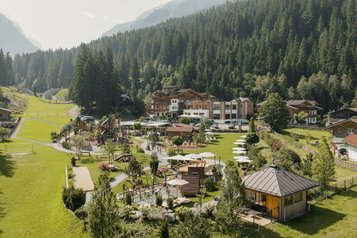 Sommerliche Außenansicht des Familienhotel Habachklause mit großem Garten, Spielplatz und umliegenden Bergen.