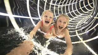 Zwei Mädchen rutschen auf dem Bauch die Röhrenrutsche im Familienhotel hinunter