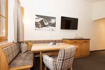 Sitz- und Essbereich im Familienzimmer des Familienhotels Oberkarteis mit gemütlicher Eckbank, Holzmöbeln und modernem Fernseher.