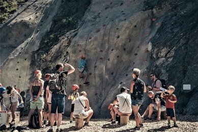 Eine Gruppe Kinder und Teens steht beim Kletterprogramm des Familienhotel Mia Alpina in Tirol vor einer Felswand.