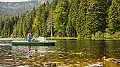 Zwei Personen fahren mit einem Tretboot auf einem See in der Natur im Bayerischen Wald.