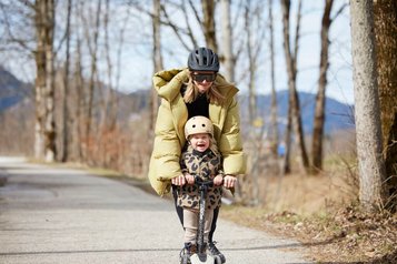 Mutter und Kind mit Helm beim Scooterfahren auf einem Weg nahe dem Familienhotel Das Bayrischzell