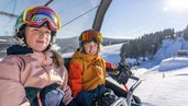 Kinder sitzen im Skilift des Familienhotels Elldus Resort im Erzgebirge.