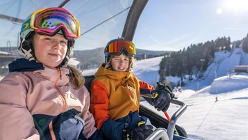 Kinder sitzen im Skilift des Familienhotels Elldus Resort im Erzgebirge.
