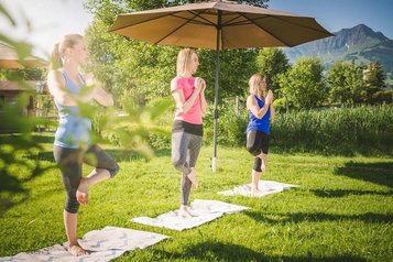 Yoga im Landgut Furtherwirt Garten, drei Frauen praktizieren Entspannungsübungen vor traumhafter Bergkulisse
