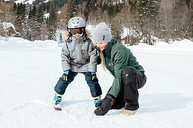 Kleiner Junge lernt im Familienhotel Post Family Resort Skifahren, die Skilehrerin unterstützt ihn dabei im Familienhotel Post Family Resort.