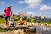 Eine Familie genießt das Spielen am erfrischenden Wasserspielplatz inmitten traumhafter Bergkulisse in Kärnten