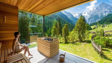 In der Sauna des Familienhotel Bella Vista in Südtirol genießt ein Gast den Blick durch große Panoramafenster auf die Berge.