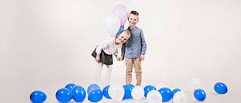Ein Mädchen und ein Junge freuen sich über viele Luftballons.