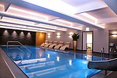Elegantes Hallenbad im Familienhotel Amiamo im Salzburger Land mit blau beleuchtetem Pool, stilvollen Liegestühlen und modernem Ambiente für entspannte Wellnessmomente.
