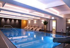 Elegantes Hallenbad im Familienhotel Amiamo im Salzburger Land mit blau beleuchtetem Pool, stilvollen Liegestühlen und modernem Ambiente für entspannte Wellnessmomente.