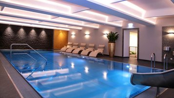 Elegantes Hallenbad im Familienhotel Amiamo im Salzburger Land mit blau beleuchtetem Pool, stilvollen Liegestühlen und modernem Ambiente für entspannte Wellnessmomente.