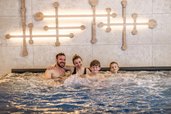 Familie entspannt gemeinsam im sprudelnden Whirlpool des Zauchenseehof, vor einer modernen Wandgestaltung mit warmem Lichtakzent.