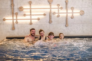Familie entspannt gemeinsam im sprudelnden Whirlpool des Zauchenseehof, vor einer modernen Wandgestaltung mit warmem Lichtakzent.