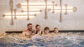 Familie entspannt gemeinsam im sprudelnden Whirlpool des Zauchenseehof, vor einer modernen Wandgestaltung mit warmem Lichtakzent.