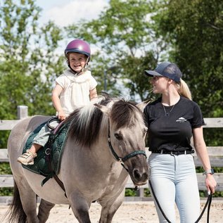 Kind reitet lachend auf einem Pony während des Reitunterrichts in der Familotel Erlebniswelt Reiten.