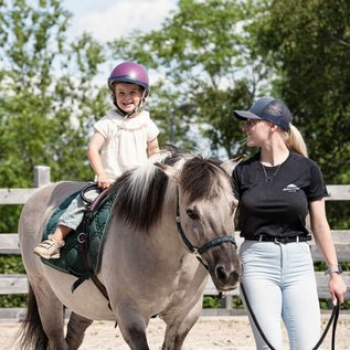 Kind reitet lachend auf einem Pony während des Reitunterrichts in der Familotel Erlebniswelt Reiten.