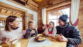 Familie in einer Skihütte in Tirol beim Mittagessen. Auf dem Tisch steht traditioneller Kaiserschmarren.