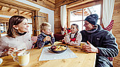 Familie in einer Skihütte in Tirol beim Mittagessen. Auf dem Tisch steht traditioneller Kaiserschmarren.