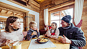 Familie in einer Skihütte in Tirol beim Mittagessen. Auf dem Tisch steht traditioneller Kaiserschmarren.