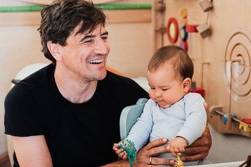 Vater spielt mit seinem Baby im liebevoll gestalteten Spielzimmer des Familienhotels Tirolerhof.