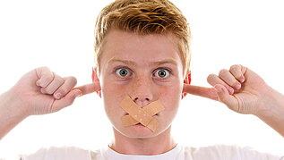Ein Junge hält sich die Ohren zu und hat ein Pflaster über den Mund