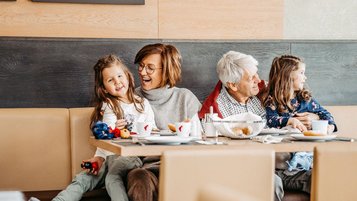 Großeltern sitzen mit zwei Mädchen am gedeckten Frühstückstisch im AIGO Welcome Family.