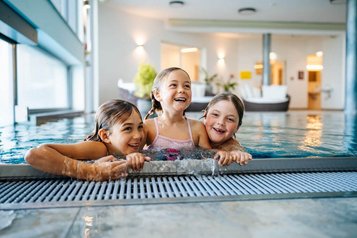 Drei lachende Kinder spielen gemeinsam im Indoor-Pool des Familien Resort Petschnighof in Kärnten.