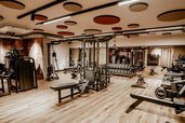 Heller Fitnessraum im Familienhotel Mia Alpina in Tirol mit Kraftgeräten, Hanteln, Trainingsbank und Holzboden.