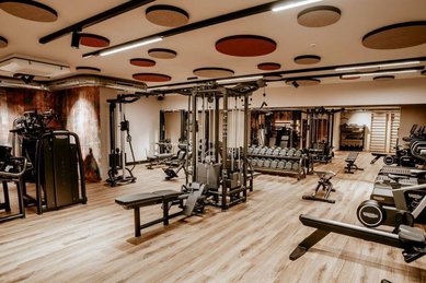 Heller Fitnessraum im Familienhotel Mia Alpina in Tirol mit Kraftgeräten, Hanteln, Trainingsbank und Holzboden.