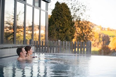 Eltern im Infinitypool des Landhaus zur Ohe im Bayerischen Wald blicken auf eine herbstliche Landschaft.