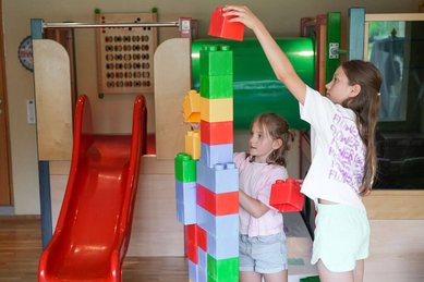 Zwei Kinder bauen gemeinsam einen hohen Turm aus großen bunten Bausteinen im Spielbereich des Familienhotel Sonne Bezau.