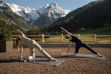 Yoga auf der Terrasse des Familienhotel Bella Vista in Südtirol mit Blick auf Wiesen, Berge und verschneite Gipfel.