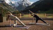 Yoga auf der Terrasse des Familienhotel Bella Vista in Südtirol mit Blick auf Wiesen, Berge und verschneite Gipfel.