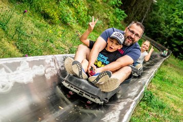 Eine Familie fährt eine Sommerrodelbahn in der Nähe des Familienhotels Rhön Feeling hinab.