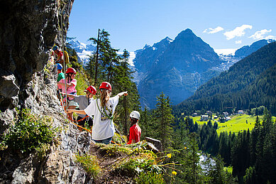 Kinder klettern an einer Steinwand hoch.