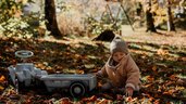Ein Kind sitz am Boden im Blätterlaub im Herbst im Familienhotel Post Family Resort im Salzburger Land.