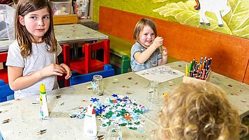 Zwei Kinder basteln und malen an einem Tisch mit Buntstiften und Glitzer im Kinderclub des Hotels Feldberger Hof.
