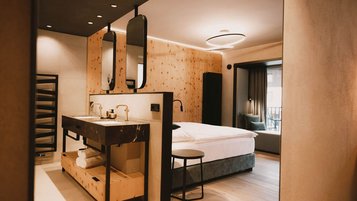Ein modernes, stilvoll eingerichtetes Zimmer im Familienhotel Kindl lädt mit warmen Holzelementen und offenem Badezimmerbereich zum Wohlfühlen ein